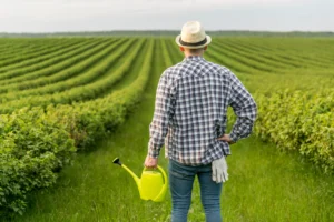 Produtor rural observando sua plantação, de costas, com regador na mão